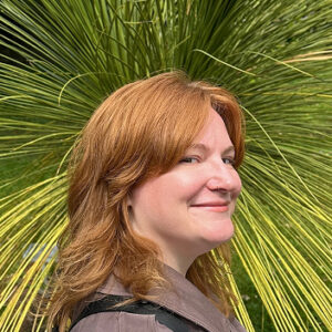 Portrait of Sarah P. Hanson, in three-quarter profile, in front of a large green plant with thin, frond-like leaves.